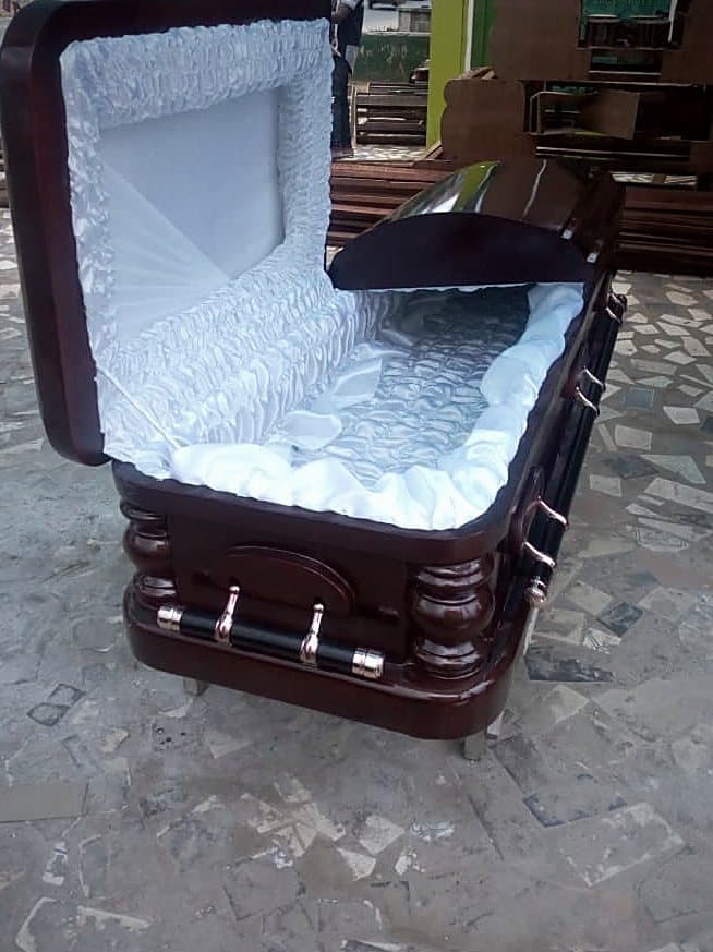 A mahogany casket standing open, showing the quilted interior and adjustable bed