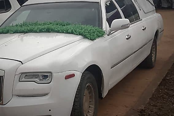 The white executive hearse in profile, dressed with a green floral garland
