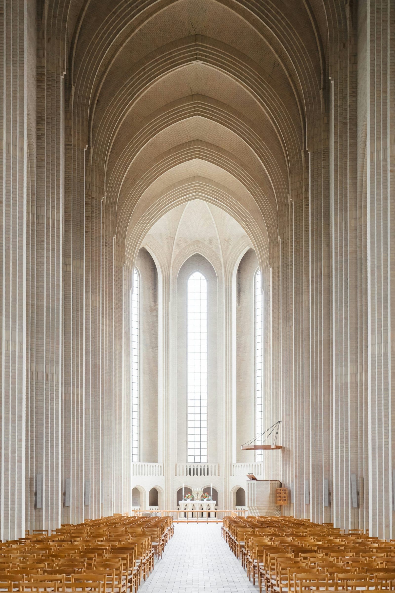 The arched nave of a church, seen down the centre aisle toward tall windows