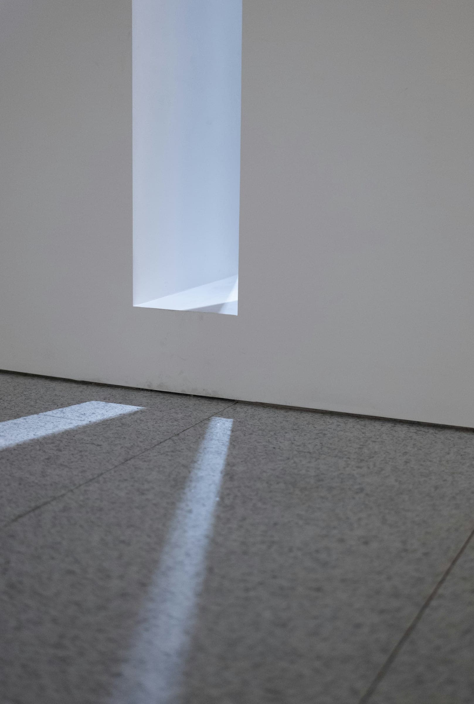 A narrow opening in a pale wall, with light falling across a stone floor