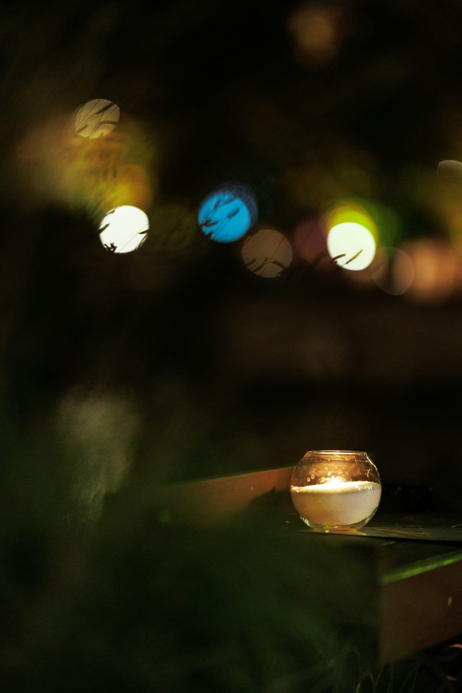 A candle burning in a glass, with soft lights out of focus behind it
