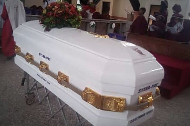 A white and gilt casket on its bier inside a church, flowers on the lid