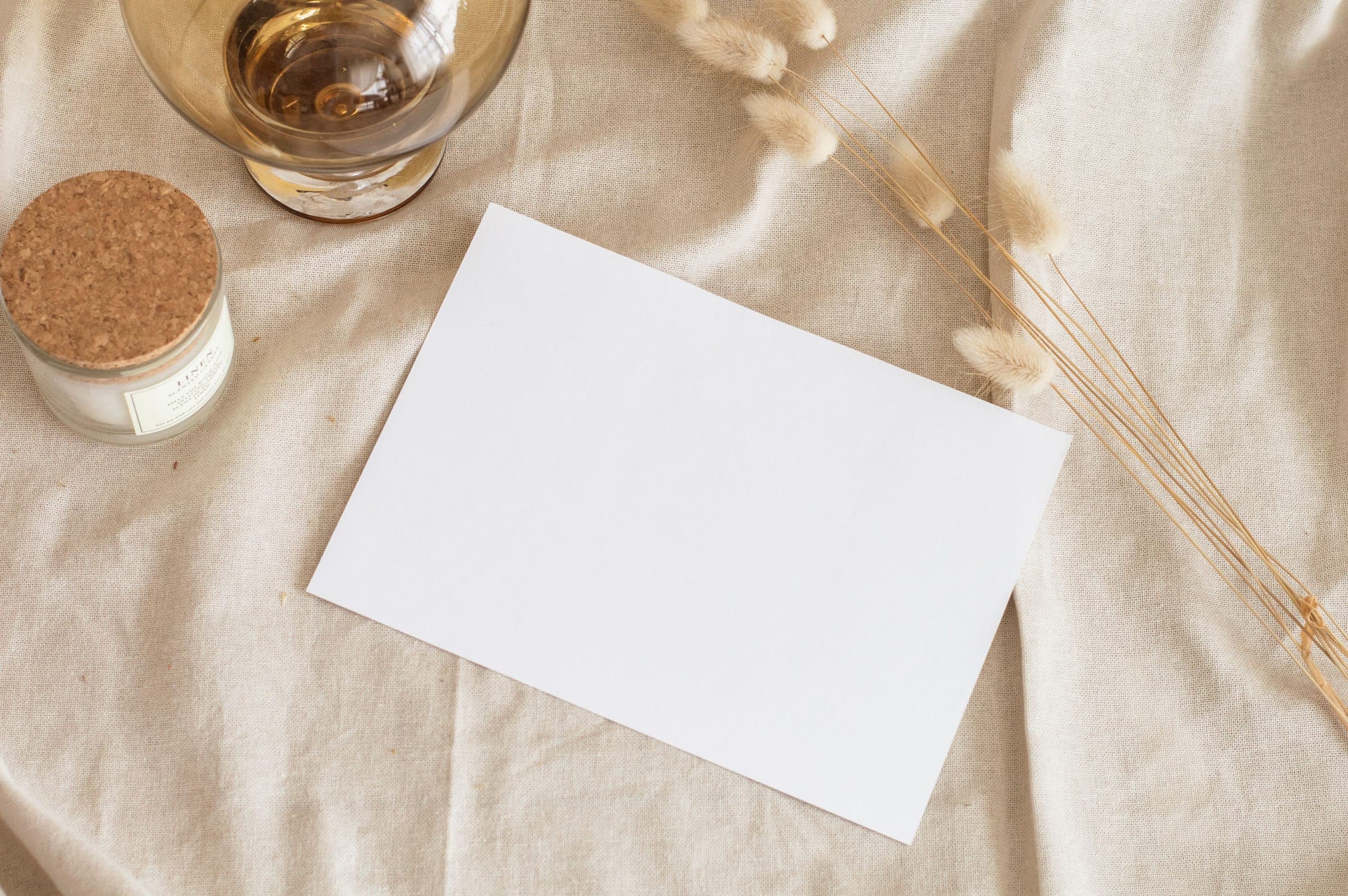 A blank card laid on linen with dried grasses beside it, seen from above